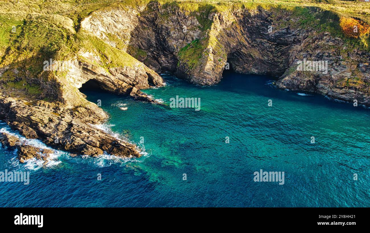 Vista aerea di una costa rocciosa con acque turchesi cristalline. Le scogliere sono aspre e verdi, con qualche vegetazione visibile. Le onde si infrangono dolcemente Foto Stock