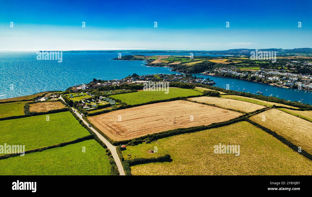 Vista aerea di un paesaggio costiero caratterizzato da campi, un fiume e una piccola città sul mare. La scena mostra vivaci campi verdi, una raccolta d'oro Foto Stock