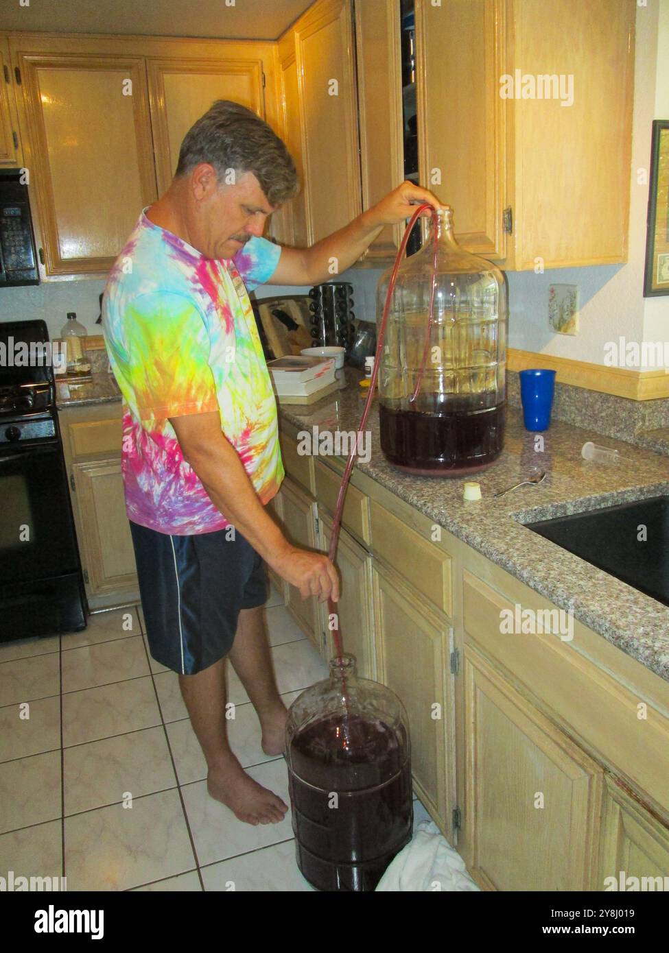 Un uomo che produce vino dalla sua uva coltivata in casa e dondola il succo Foto Stock