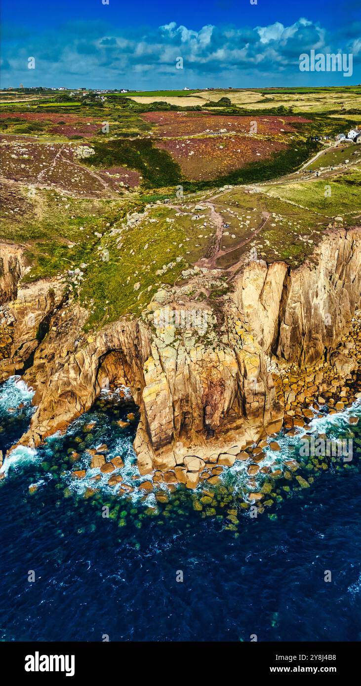 Vista aerea delle aspre scogliere che incontrano l'oceano, con lussureggianti colline verdi sullo sfondo. La costa presenta formazioni rocciose e acque cristalline Foto Stock