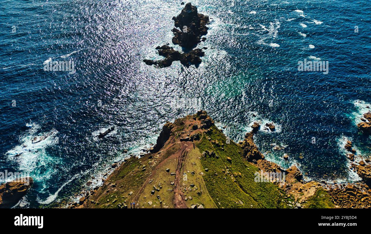 Vista aerea di una costa rocciosa con una piccola isola nell'oceano. L'acqua risplende sotto la luce del sole, creando un bellissimo contrasto con l'avidità Foto Stock