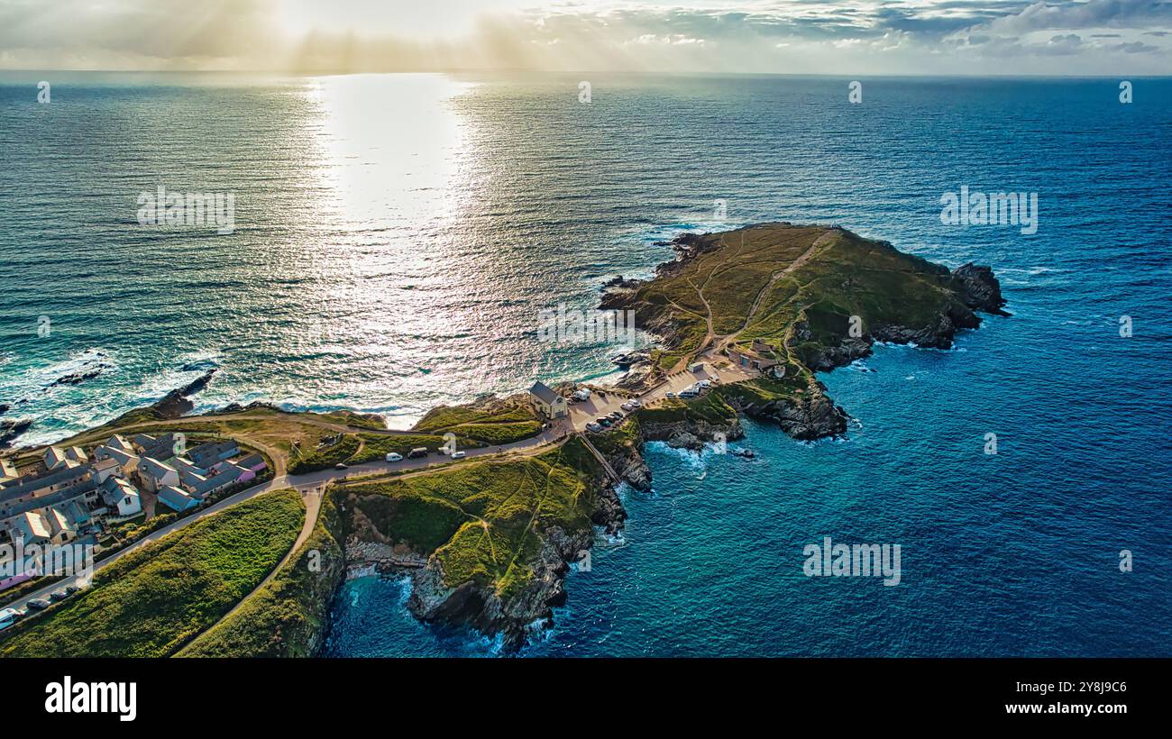 Vista aerea di un paesaggio costiero caratterizzato da una penisola che si estende fino all'oceano. Il sole sta tramontando, gettando un bagliore dorato sull'acqua. Piccolo Foto Stock