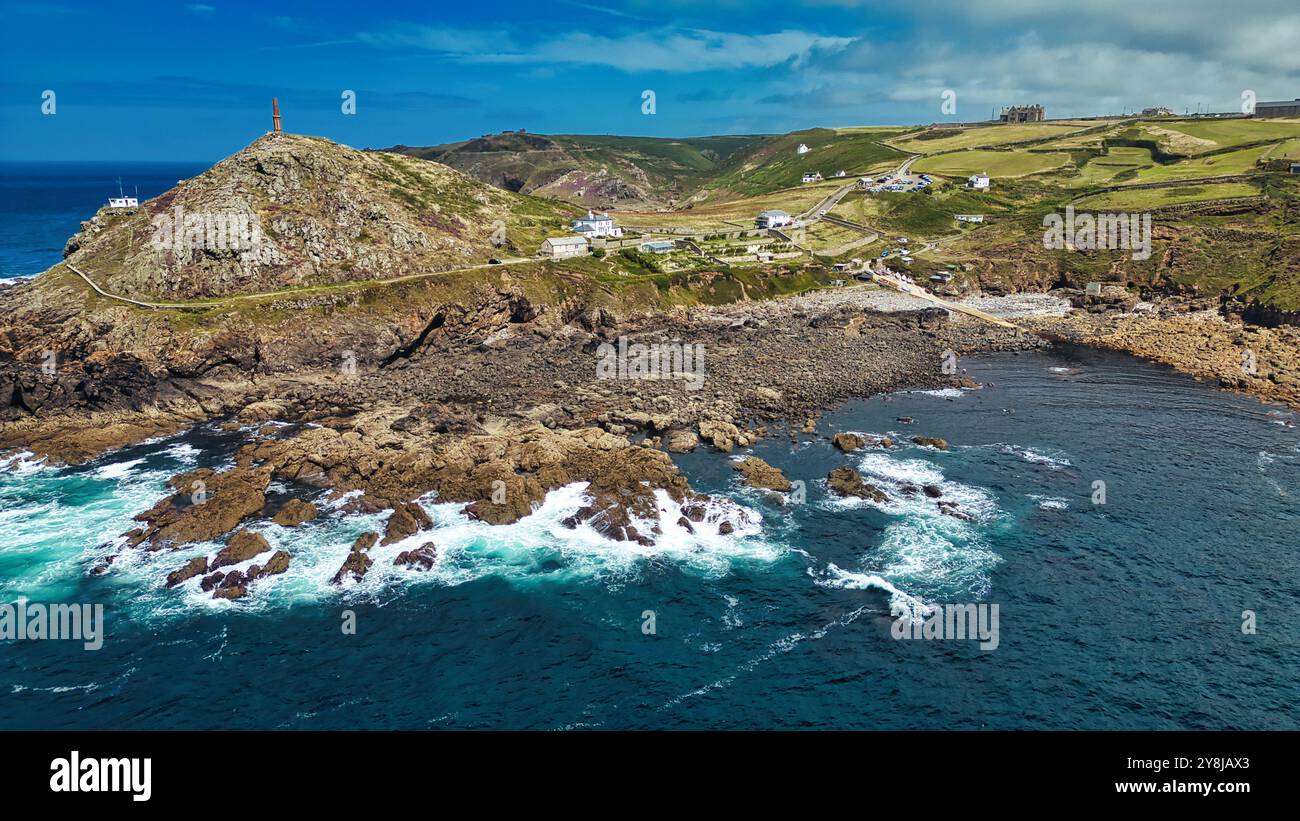 Un paesaggio costiero panoramico caratterizzato da coste rocciose, colline ondulate e un faro sulla cima di una collina. Le onde oceaniche si schiantano contro le rocce, con un chiaro Foto Stock