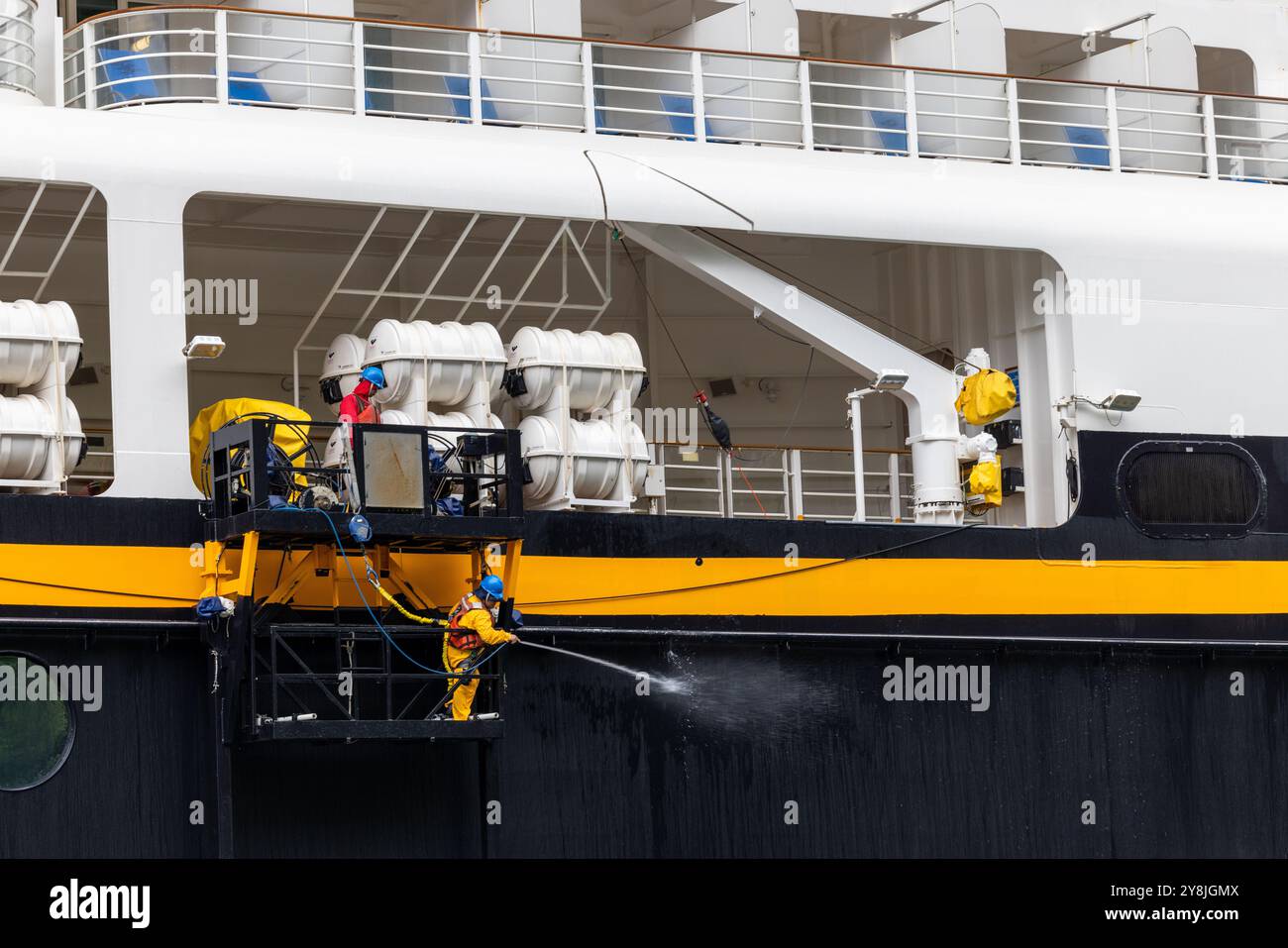 Nave da crociera Disney 15 agosto 2024 - Un operaio su una piattaforma sta lavando a pressione il lato di una grande barca Foto Stock