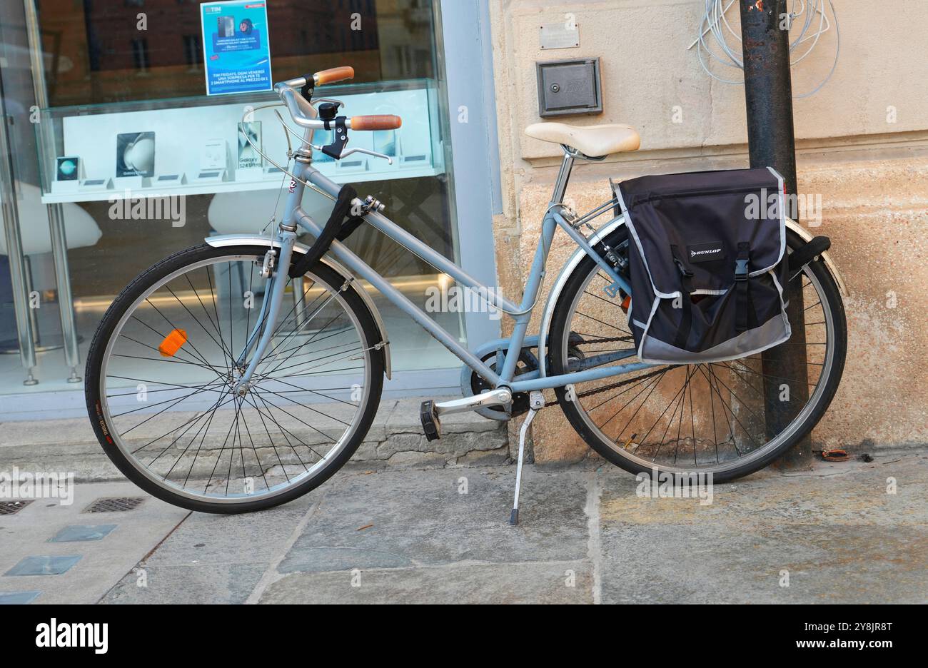 Una classica bicicletta da pendolare blu chiaro con passaggio anteriore equipaggiata con una borsa posteriore nera è parcheggiata su un marciapiede di pietra a Parma, Italia. Foto Stock