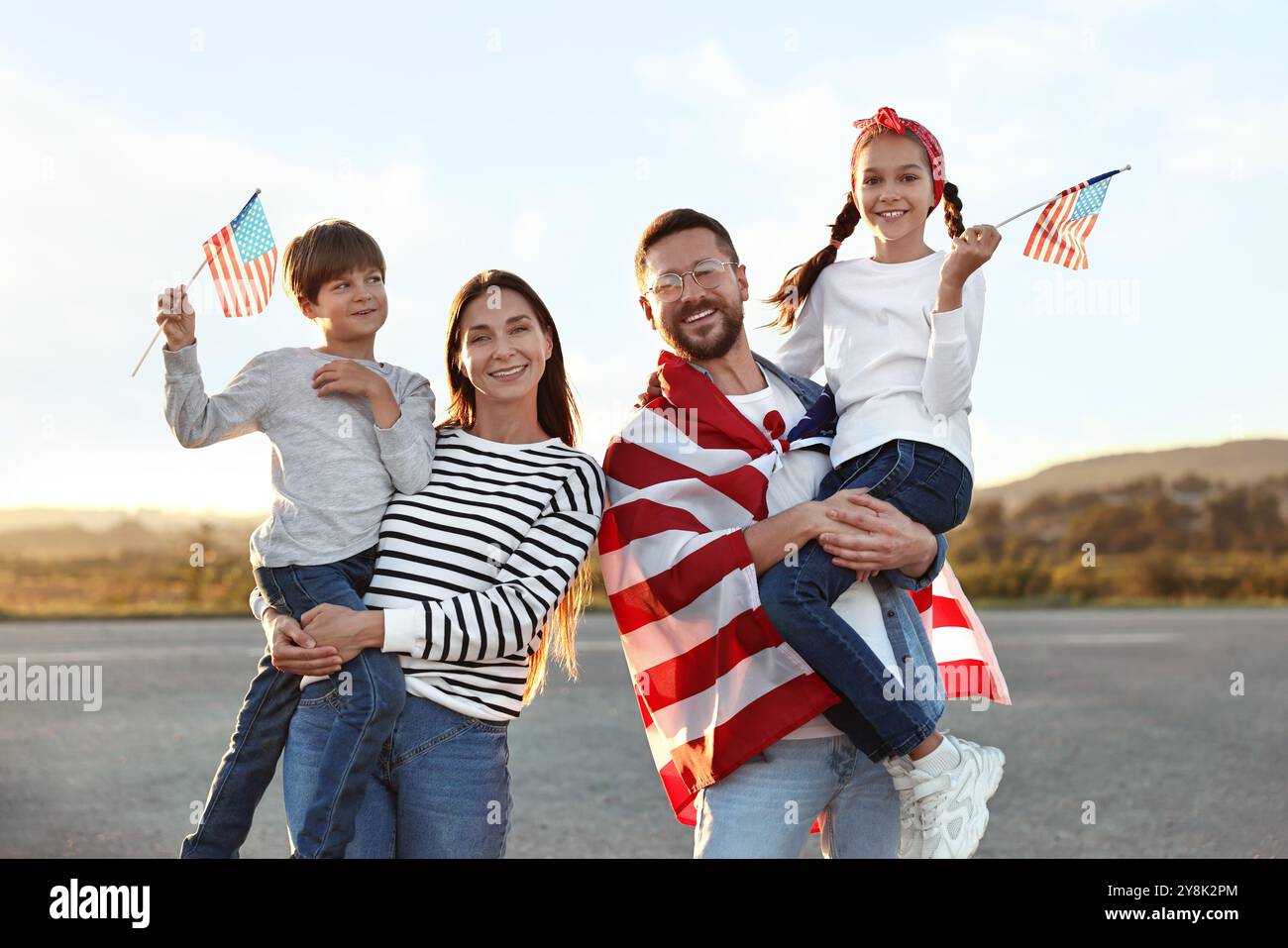 Ritratto di famiglia di genitori felici con bambini che sventolano bandiere USA all'aperto Foto Stock