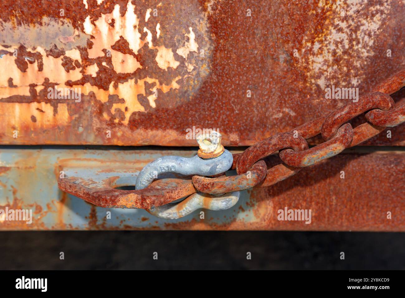 Fotografia di un vecchio arco D Bolt collegato a una catena arrugginita su un grande contenitore metallico marrone e arrugginito. Foto Stock