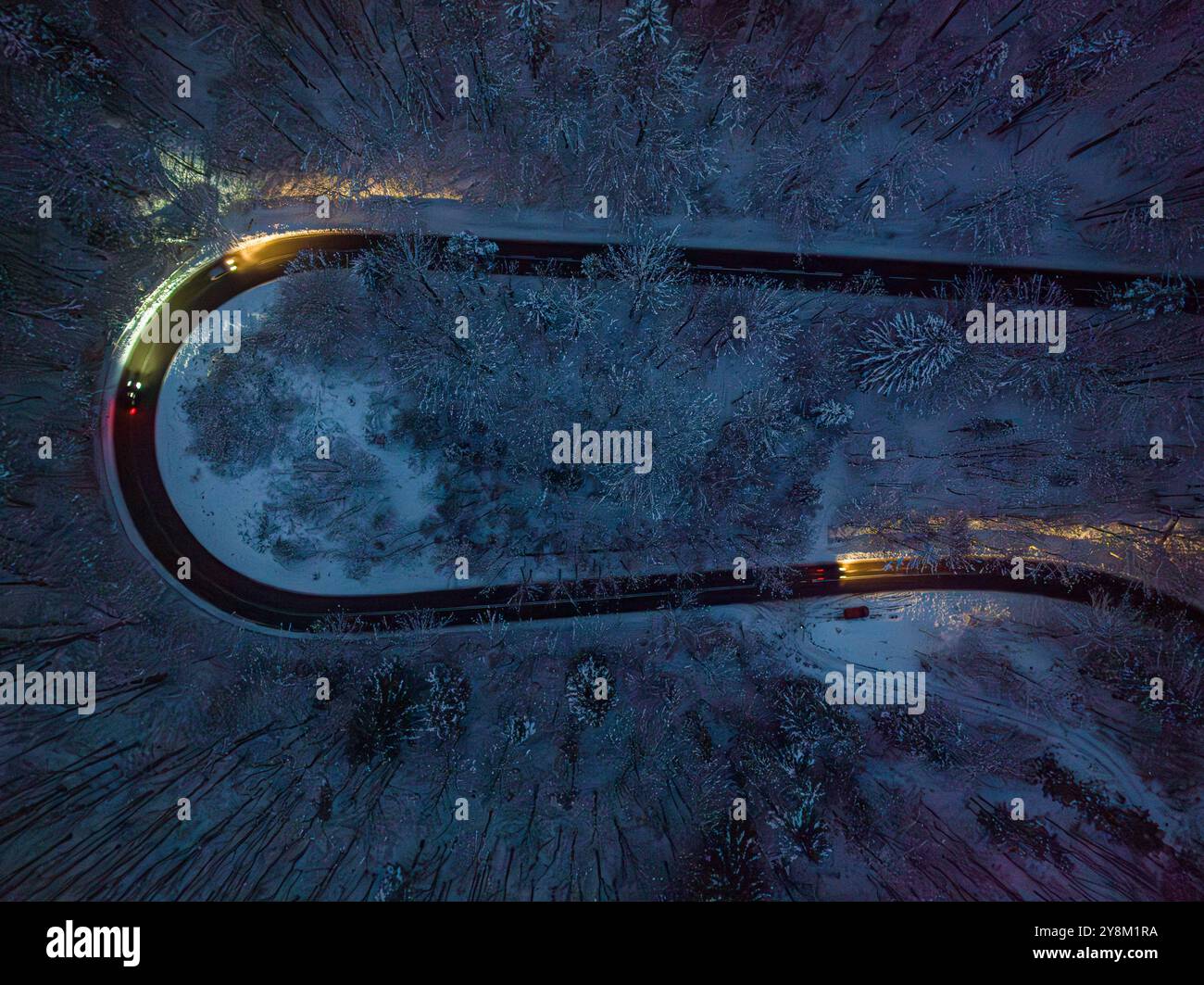 Fari dell'auto illuminano la strada tortuosa dopo il buio in inverno. Trasporto notturno in inverno. Foto Stock