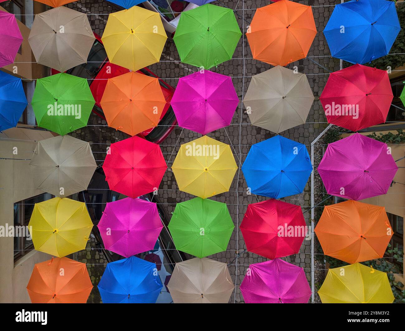 Vivace esposizione sopraelevata di ombrelli multicolori appesi tra due edifici in uno stretto cortile urbano a Łódź, Polonia Foto Stock