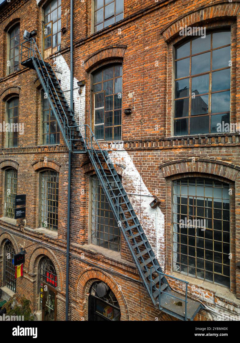 Edificio industriale in mattoni con scala in metallo e finestre d'epoca a Łódź, che cattura il patrimonio architettonico urbano e la rivitalizzazione artistica Foto Stock