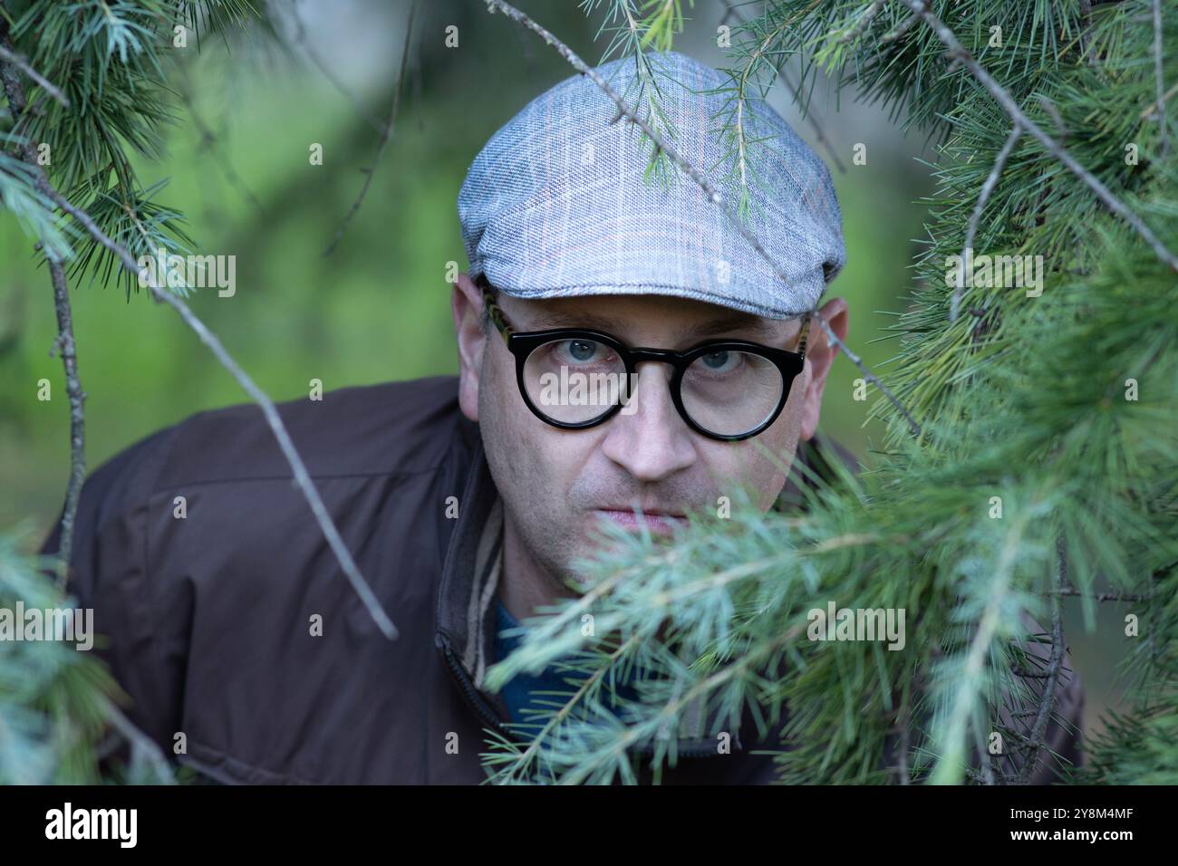 Uno stalker inquietante che si nasconde tra le piante guarda nella telecamera. Foto Stock