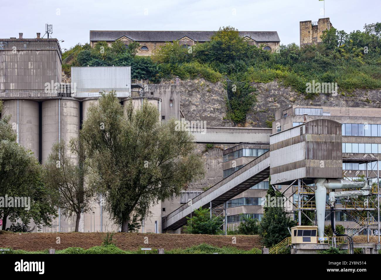 Enorme complesso industriale di una fabbrica, edificio e contenitori rotondi, rovine del castello sul monte Hoeve Lichtenberg sullo sfondo, giornata nuvolosa nel Maastrich Foto Stock