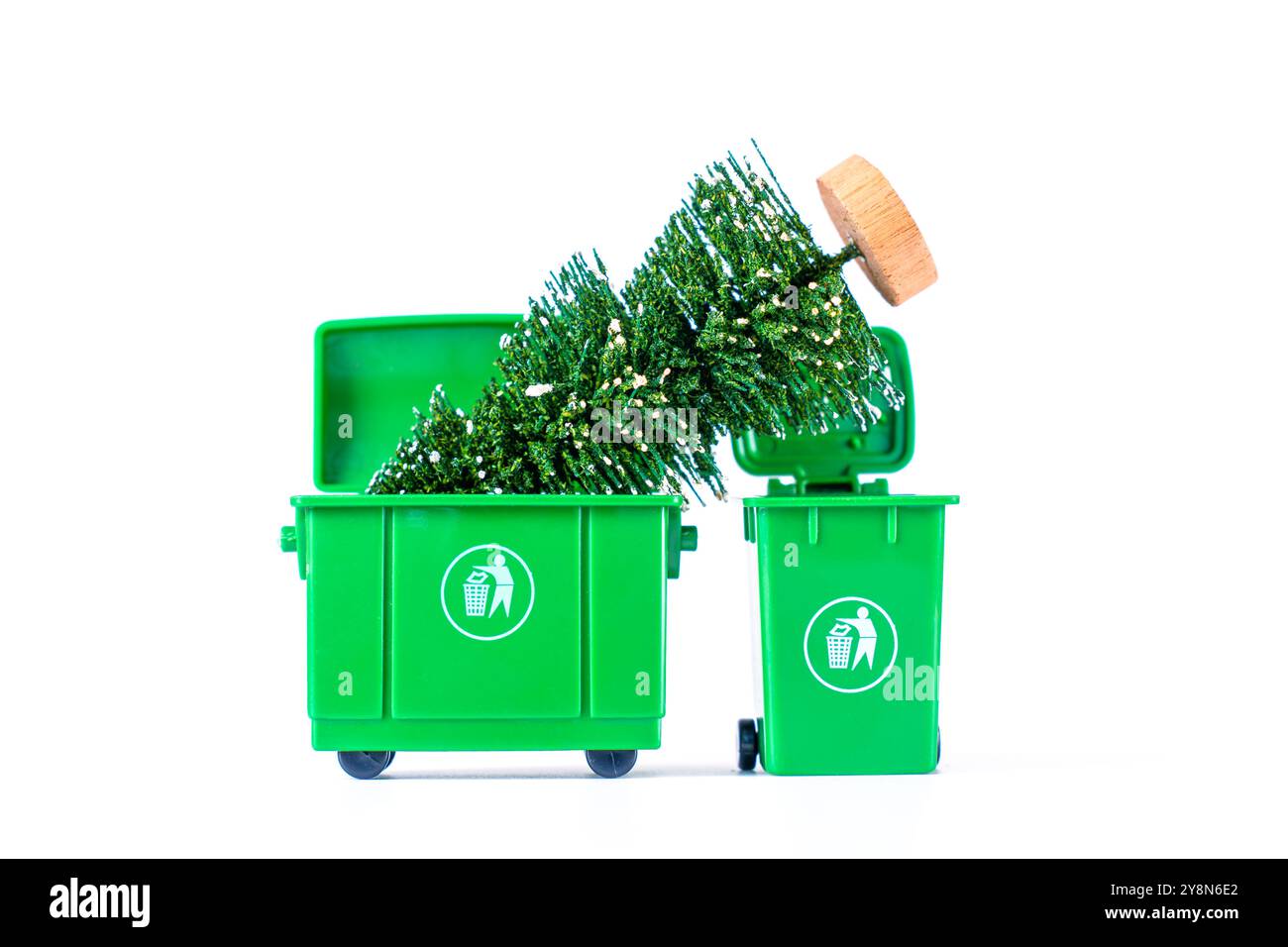 Albero di Natale artificiale con una base in legno che emerge da due cestini verdi, mettendo in risalto i temi dello smaltimento delle vacanze e della gestione dei rifiuti. Foto Stock