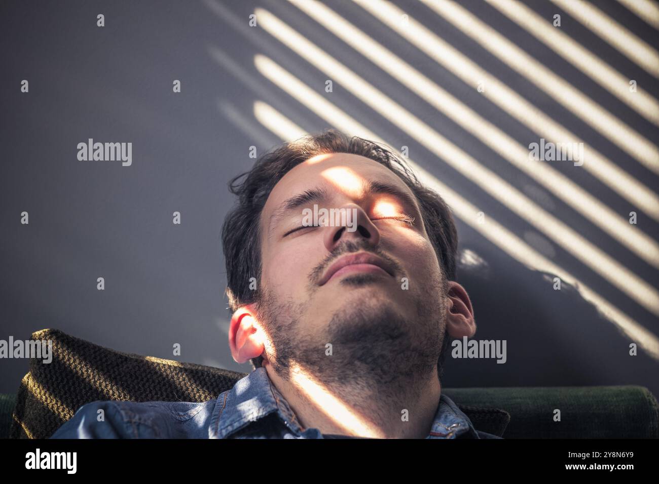 Ritratto di un uomo caucasico che si schianta sul divano, sul viso cade l'ombra dalle persiane Foto Stock