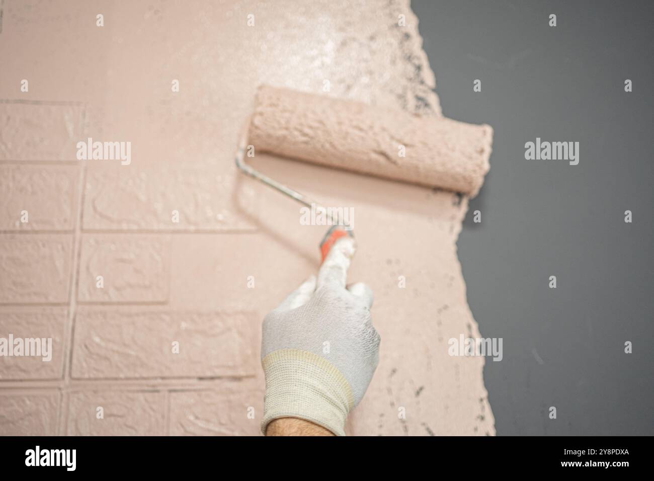 Persona che dipinge un muro in mattoni con un rullo di pittura Foto Stock