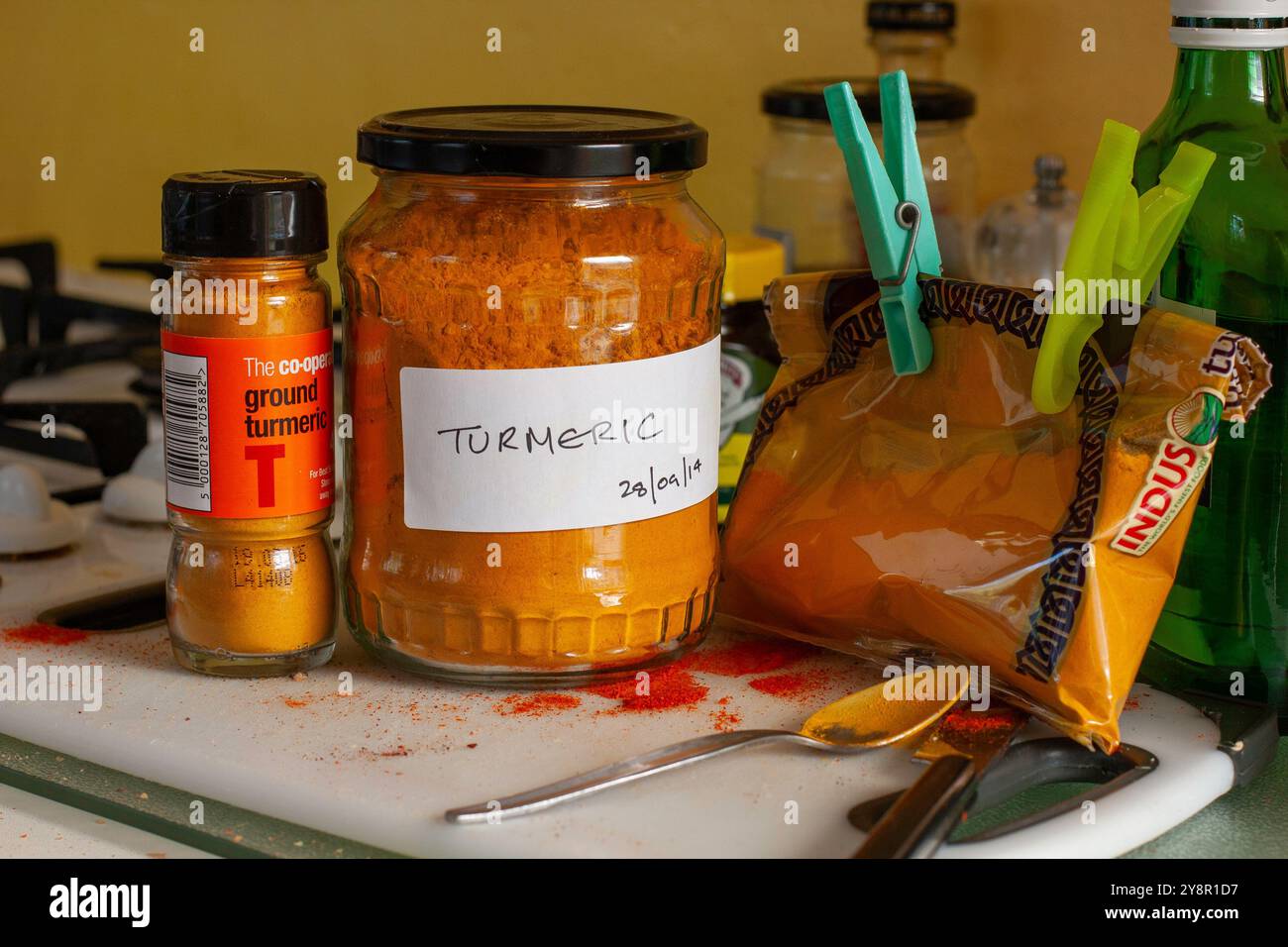 In cucina, la spezia curcuma macinata dai colori vivaci viene decantata in un grande vaso di sottaceti utilizzando un cucchiaino e alcune sono state versate sul piano di lavoro Foto Stock