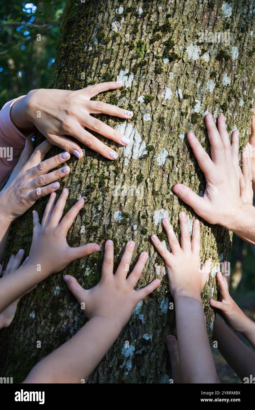 Un gruppo eterogeneo di individui in piedi insieme in natura, toccando delicatamente un albero vicino con le mani in un gesto armonioso Foto Stock