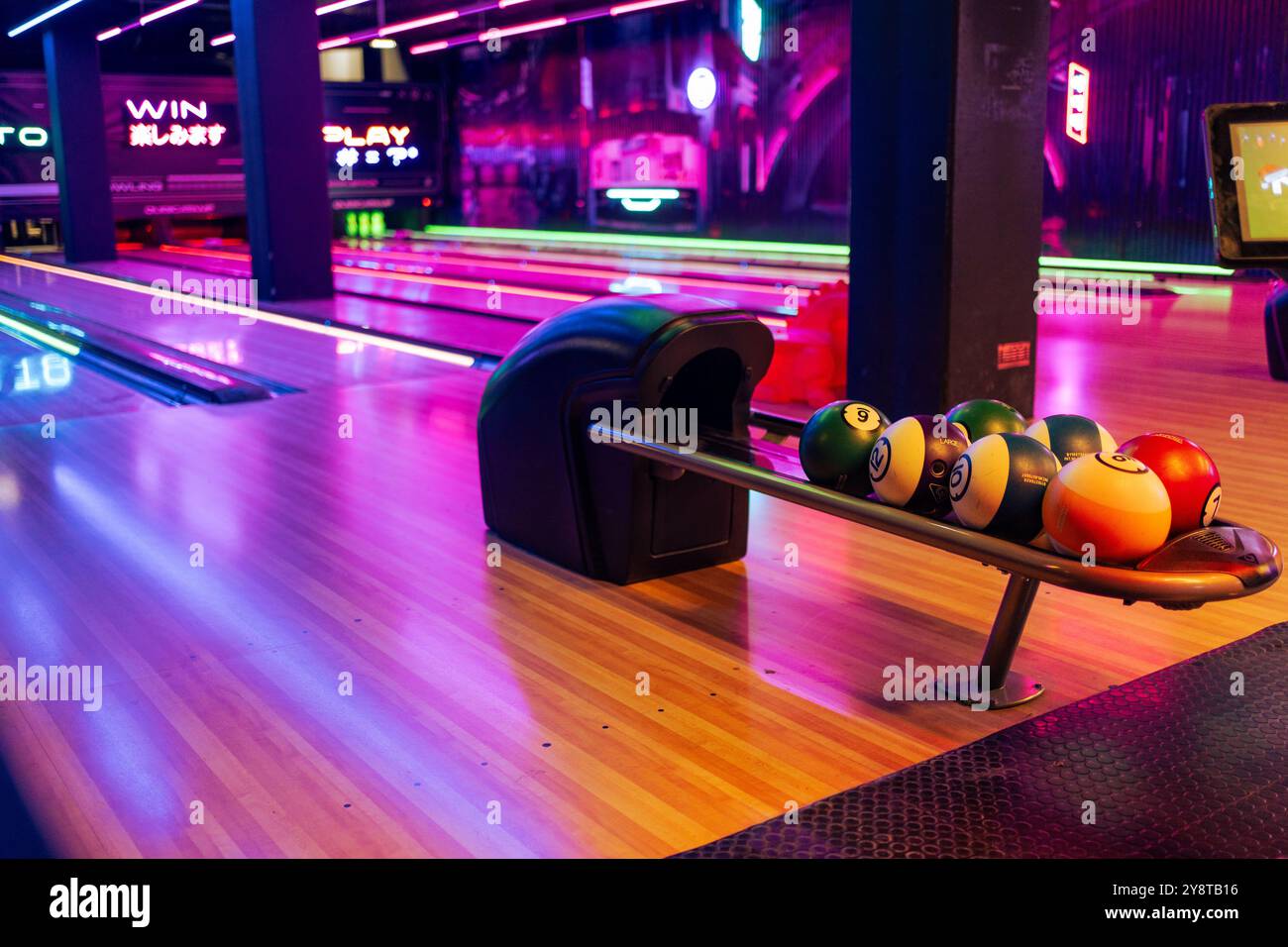 Varie palle da bowling disposte in stand con corsia di legno presso la sala da bowling. Sala giochi illuminata nel centro commerciale senza persone. Foto Stock