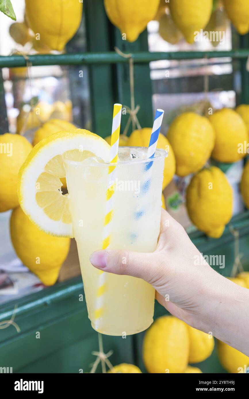 Mano caucasica con limonata fresca sana durante l'estate con sfondo di limoni Foto Stock