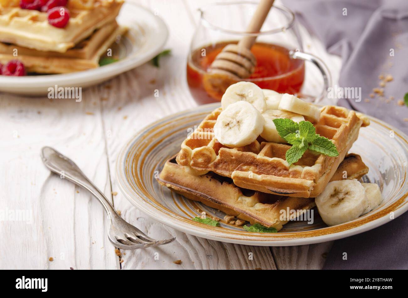 Waffle belgi serviti con banana e foglia di menta su bianco tavolo da cucina in legno con sciroppo da parte Foto Stock