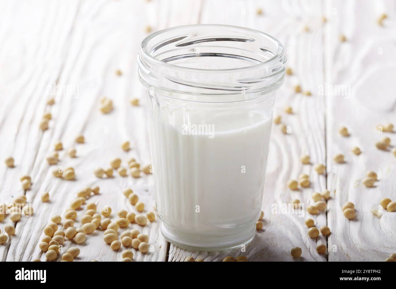 Non a base di latte di soia alternativa latte o yogurt a mason jar bianco sul tavolo di legno con i fagioli di soia a parte Foto Stock