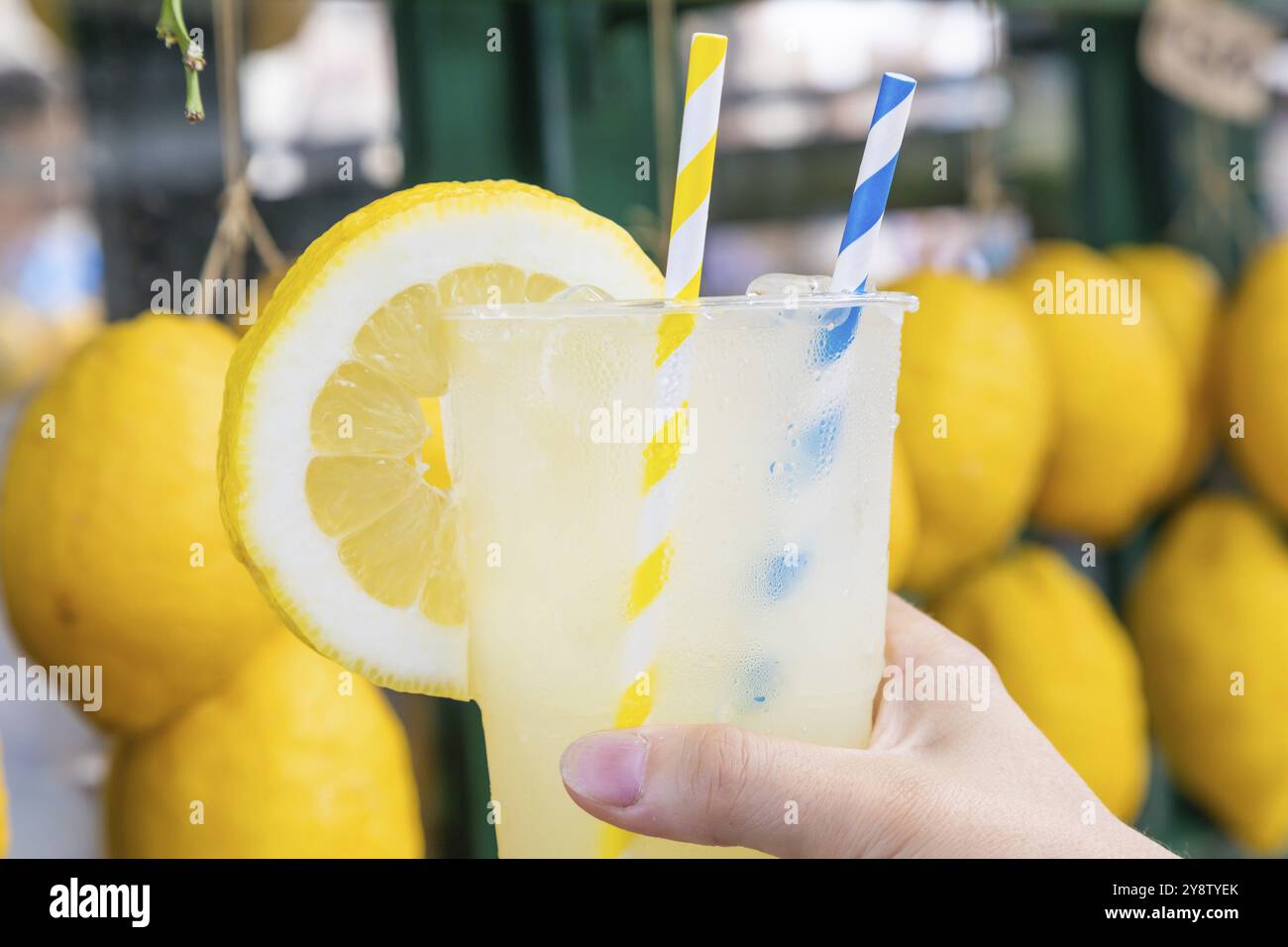 Mano caucasica con limonata fresca sana durante l'estate con sfondo di limoni Foto Stock