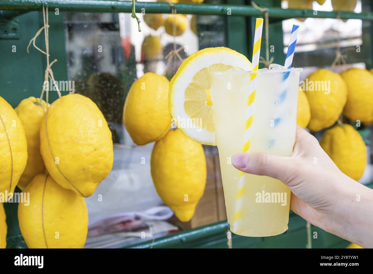 Mano caucasica con limonata fresca sana durante l'estate con sfondo di limoni Foto Stock