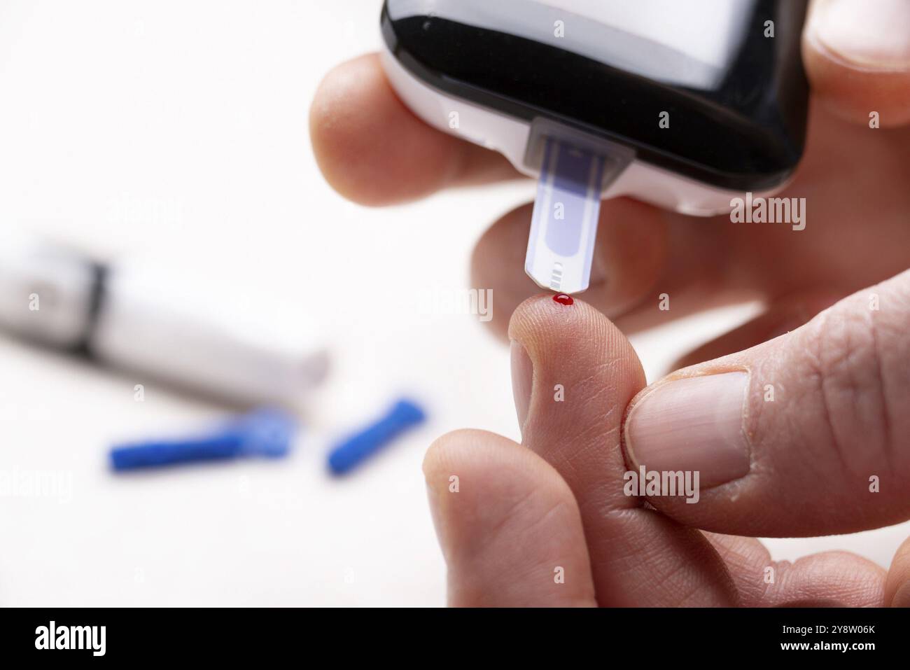 Dita caucasiche con gocce di sangue pronte per il test del glucosio a domicilio con vista ravvicinata del glucometro Foto Stock