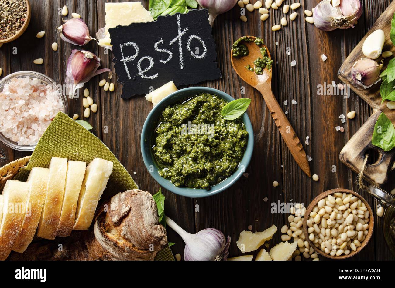 Vista piatta sullo sfondo del cibo con salsa di pesto genovese e i suoi ingredienti su un tavolo da cucina in legno che rappresenta la cucina mediterranea Foto Stock