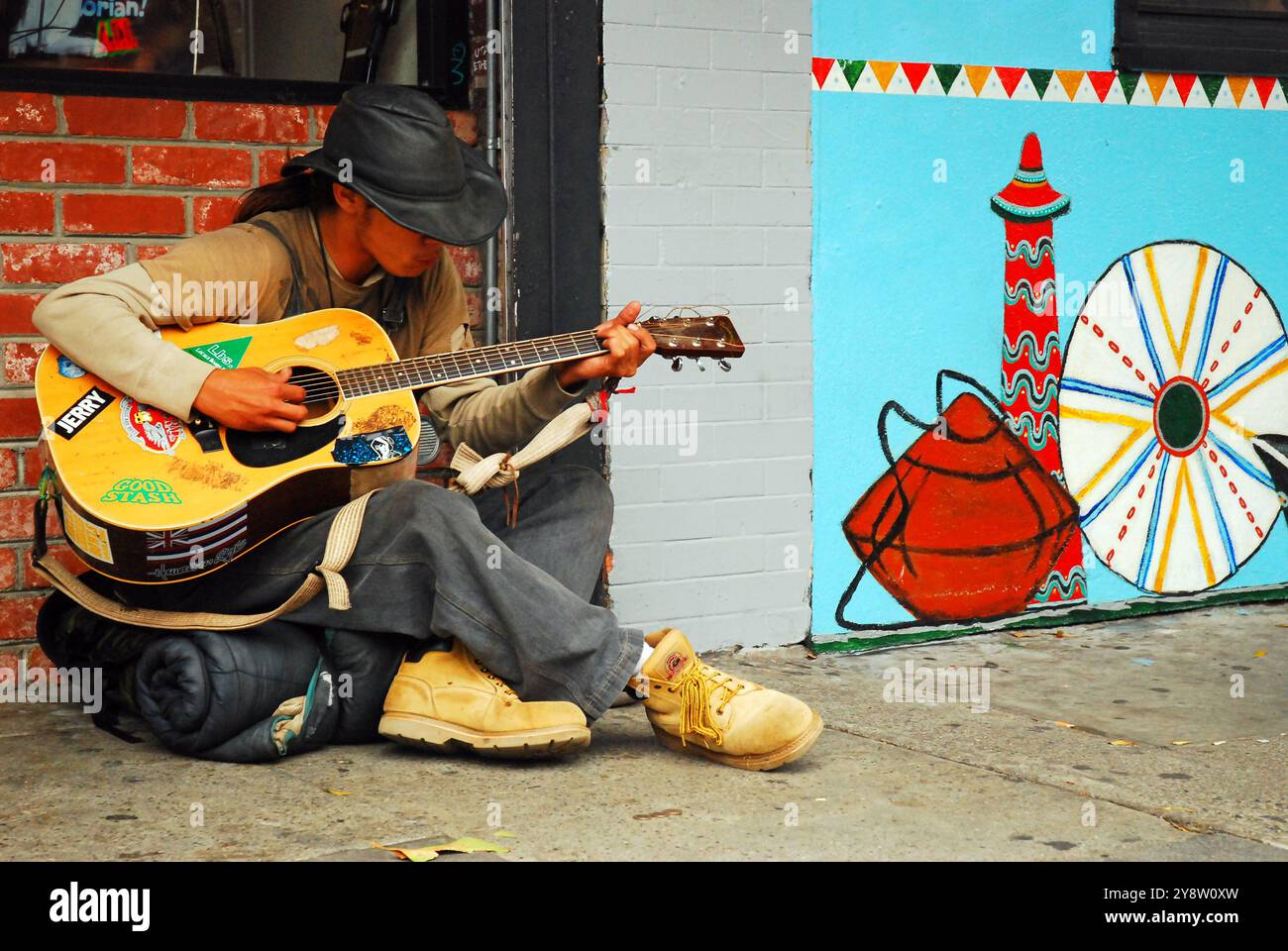 Un giovane posiziona la chitarra mentre siede sul marciapiede nel quartiere Haight Ashbury di San Francisco Foto Stock