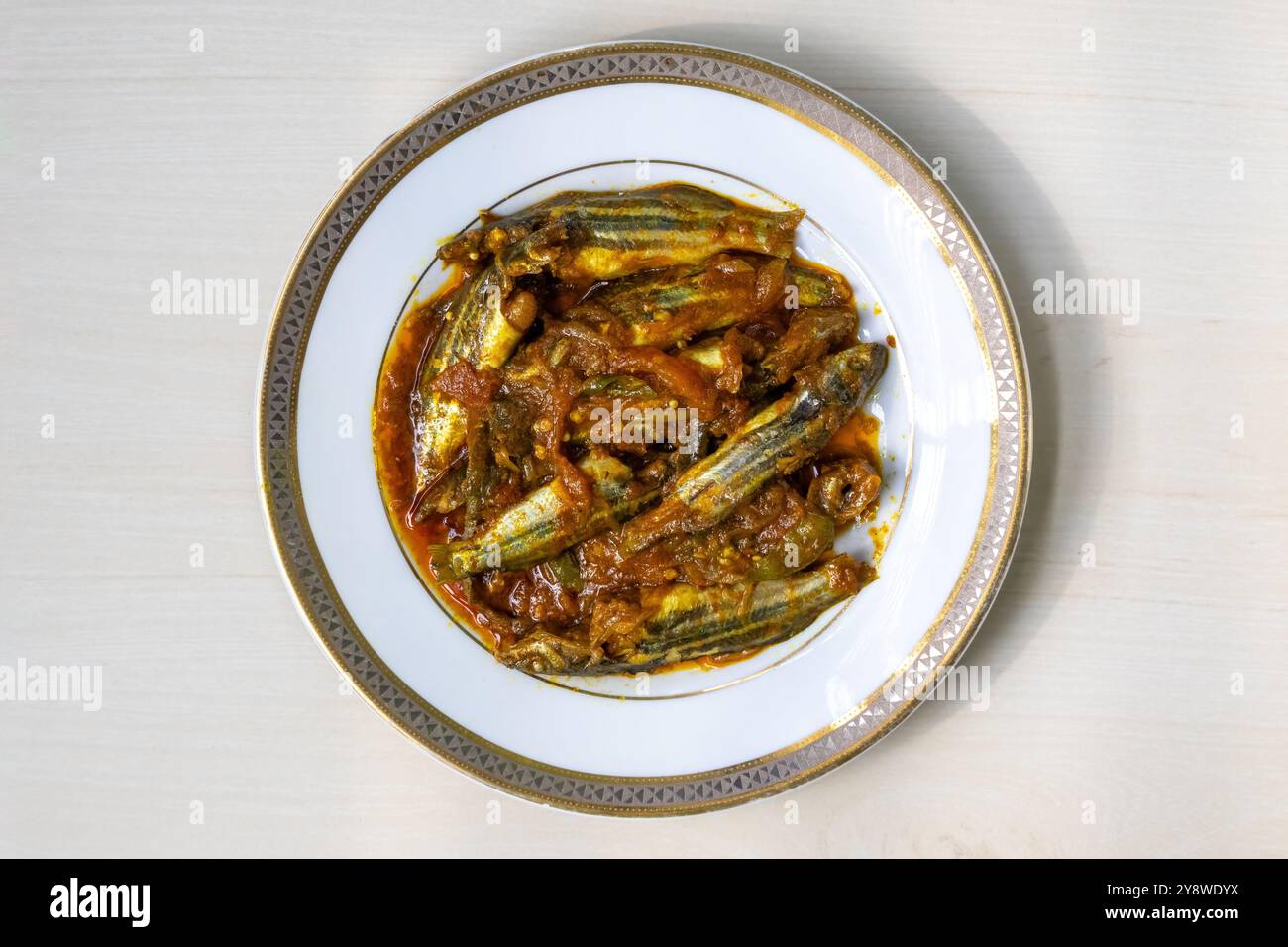 Delizioso pesce tengra cucinato e servito in un piatto bianco su uno sfondo di legno chiaro. È anche conosciuto come il Gangetic Mystus o Mystus Tengara. Superiore Foto Stock