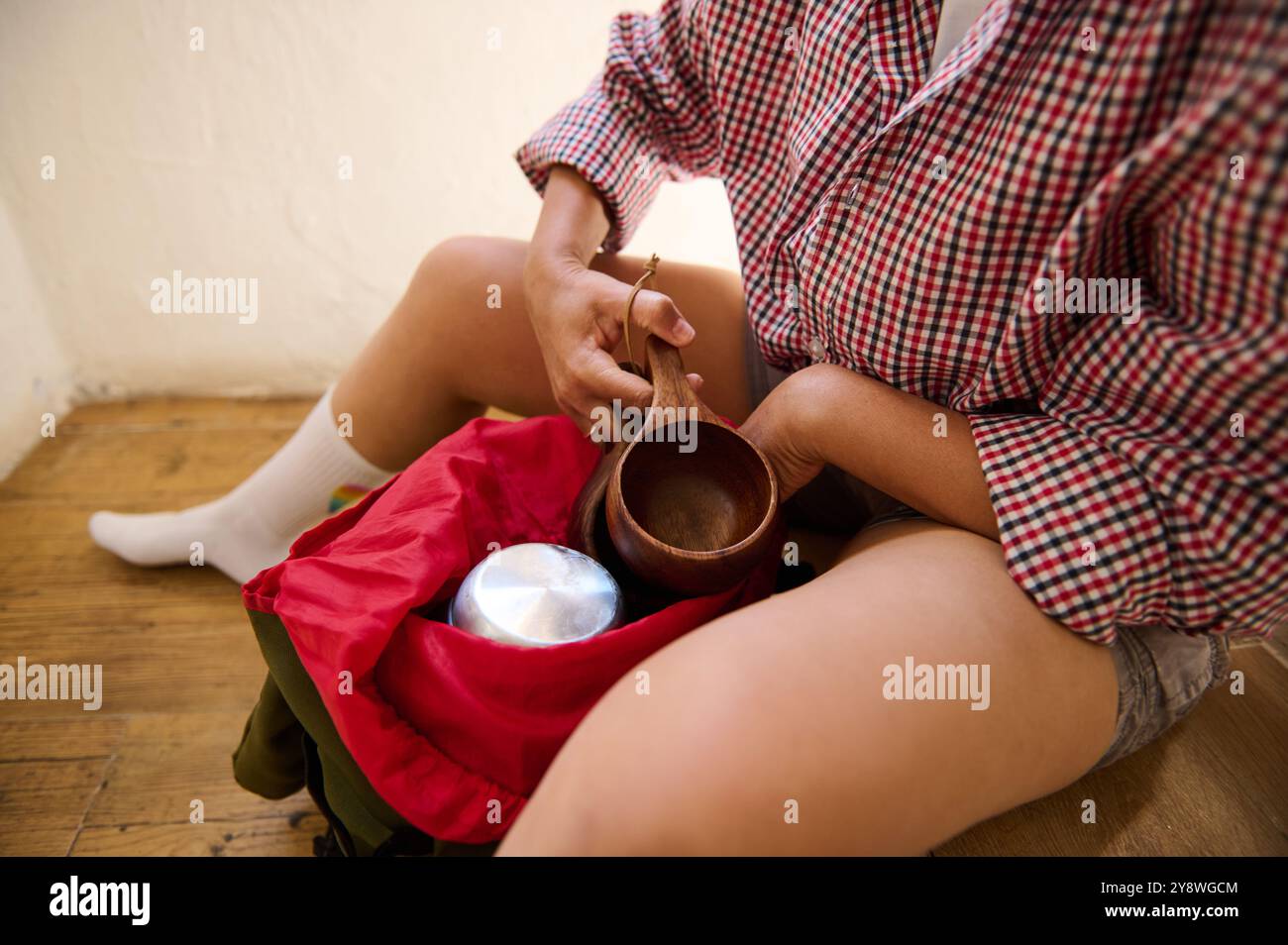 Persona che trasporta l'attrezzatura da campeggio, tra cui una tazza di legno e un contenitore di metallo in uno zaino. Atmosfera informale e avventurosa. Foto Stock