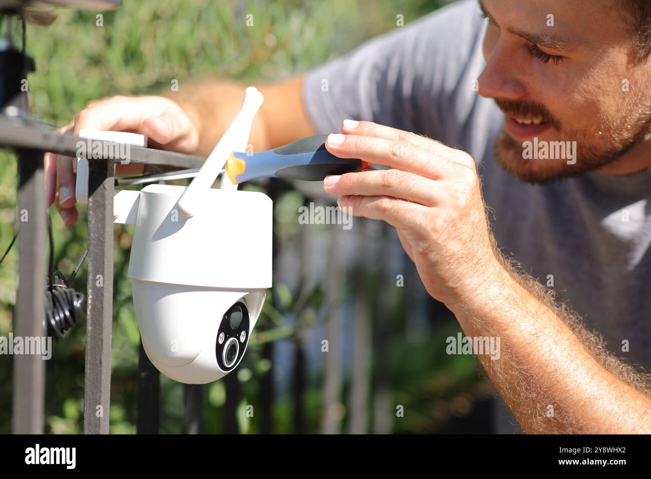 Uomo felice che installa la telecamera di sicurezza wifi in un giardino di casa Foto Stock