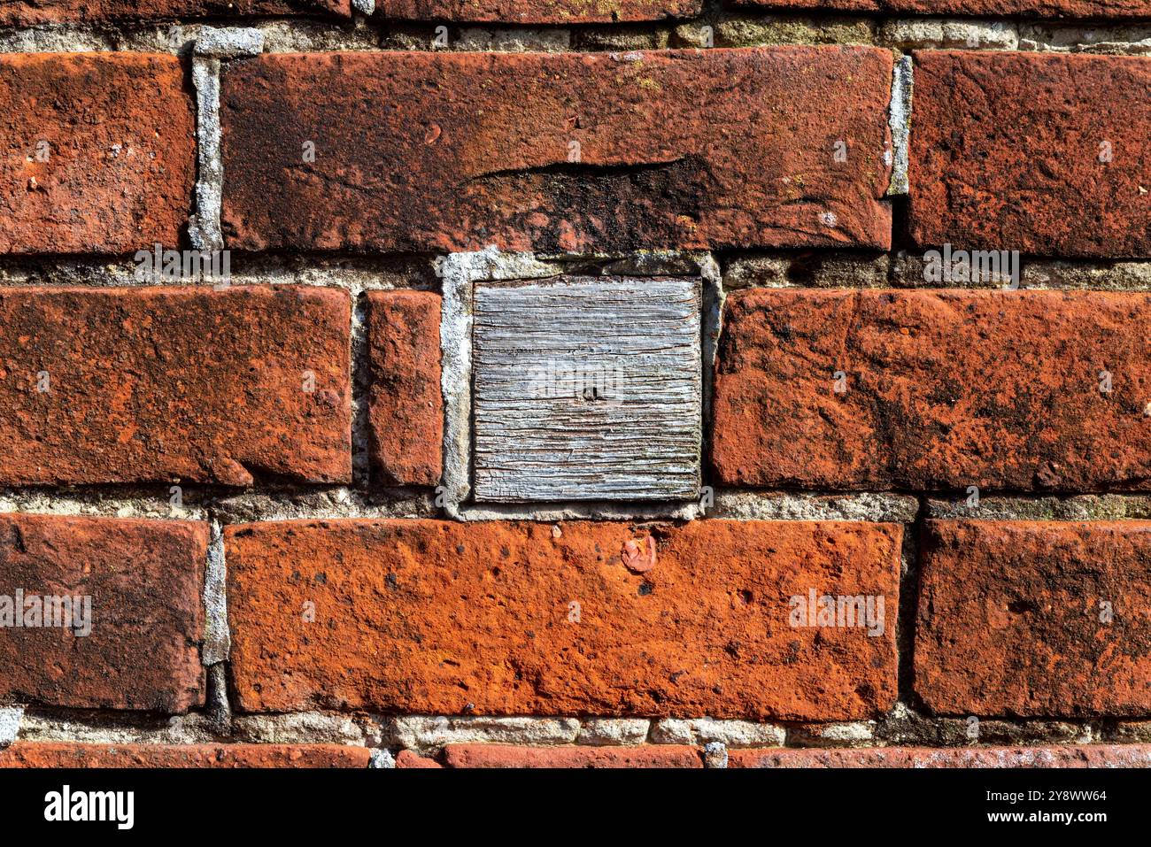 Un blocco di legno è stato inserito in una parete di mattoni per riempire un foro, utilizzando un'alternativa per una riparazione economica. Foto Stock