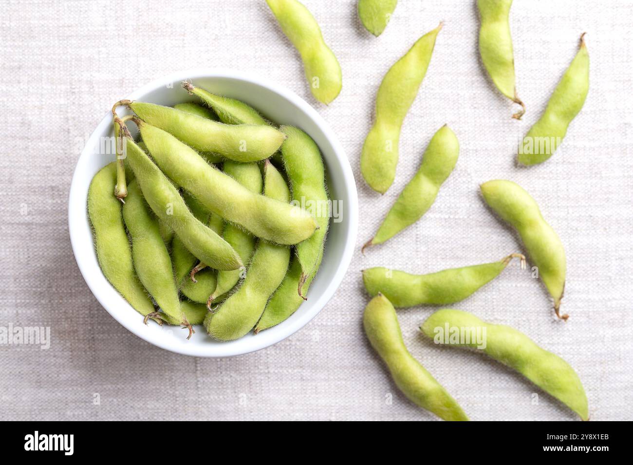 Edamame fresco, semi di soia verde nella cialda, in un recipiente bianco, su lino. Soia cruda immatura, glicina max, utilizzata bollita o al vapore e salata. Foto Stock