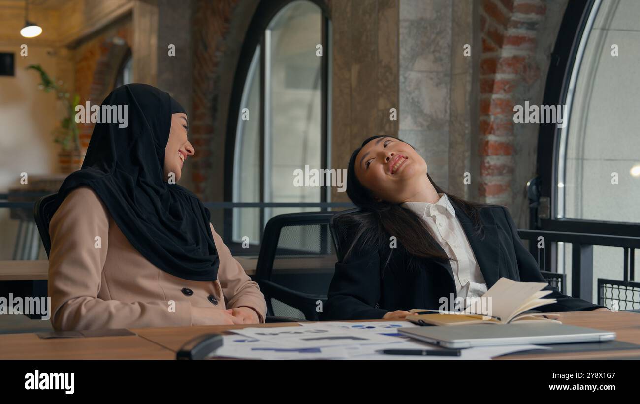 Due donne d'affari multirazziali donna asiatica coreana ragazza musulmana hijab islamico donna d'affari in ufficio sorridente fine videochiamata conferenza portatile Foto Stock