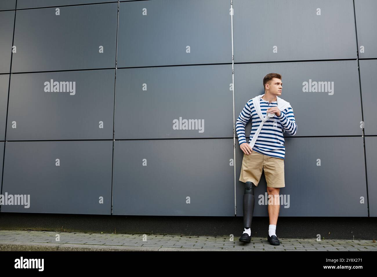 Un giovane uomo che mostra il suo stile e la sua forza unici, accanto a un elegante muro urbano. Foto Stock