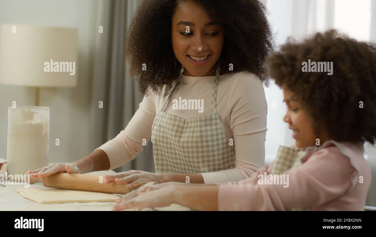 Famiglia felice in cucina cucinare insieme sorridente mamma afroamericana donna madre faccia sporca in farina bianca che insegna carino bambino figlia prescolare Foto Stock