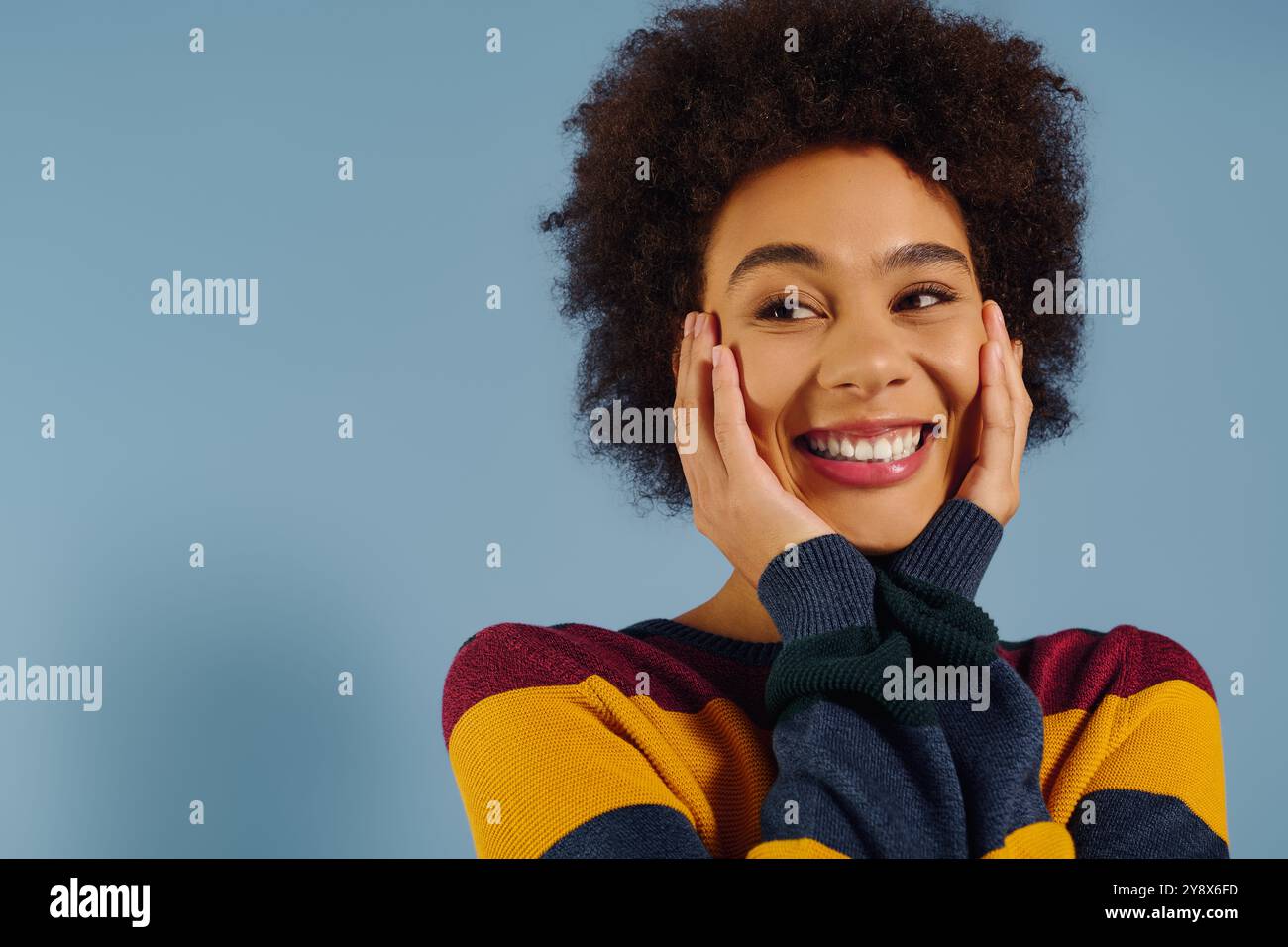 In un maglione vibrante, una giovane donna irradia di felicità, mettendo le mani sulle guance. Foto Stock