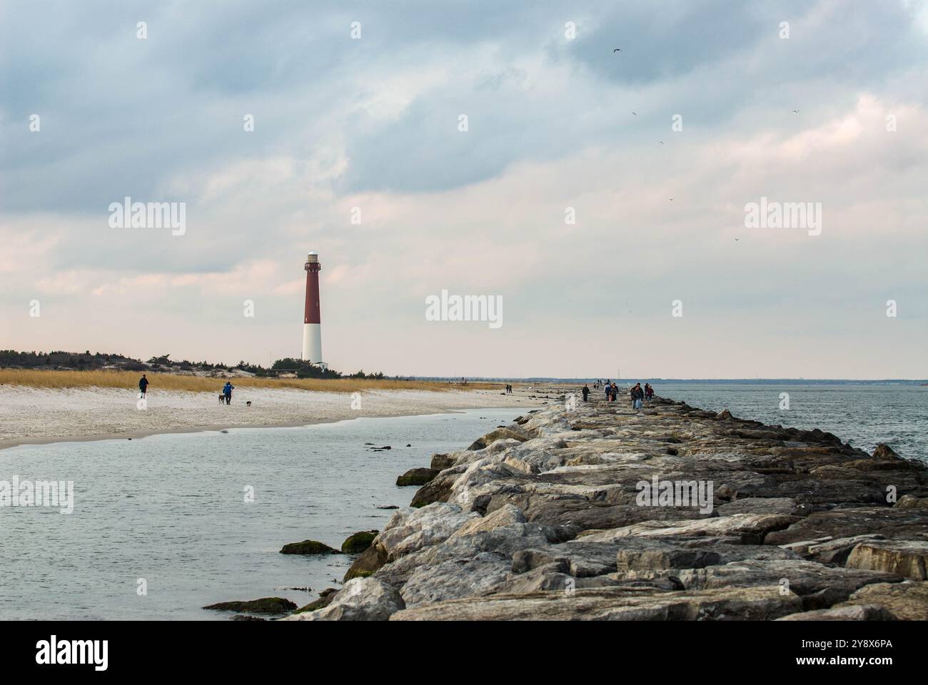 I turisti esplorano il molo di Barnegat con il faro in lontananza Foto Stock