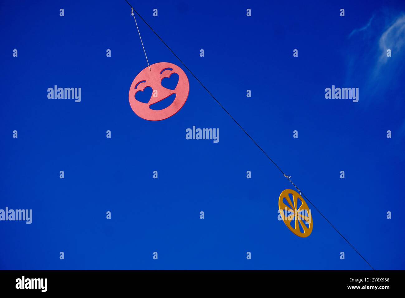 Due oggetti sospesi , un emoji arancione sorridente e una fetta di agrumi, contro un cielo azzurro e limpido creano una scena visivamente sorprendente Foto Stock