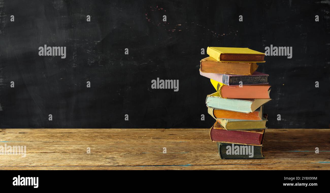 Una pila di libri con luce solare e sfondo dipinto scuro, lettura, apprendimento, conoscenza, ritorno a scuola, istruzione o concetto di ufficio domestico Foto Stock