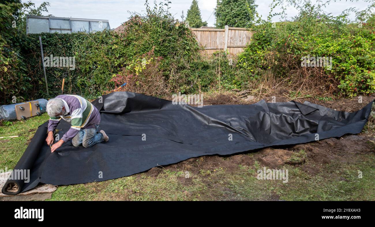 Creare e rivestire un laghetto con animali selvatici in un giardino, Regno Unito. Uomo persona che taglia le strisce di sottocopertura alla giusta lunghezza Foto Stock