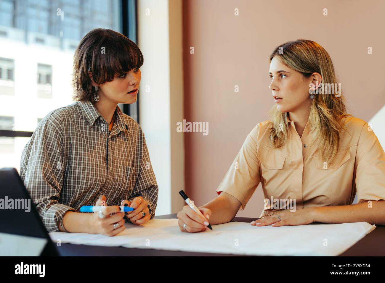 I compagni di classe condividono una discussione significativa mentre lavorano insieme a un progetto di scrittura, sottolineando la collaborazione e l'apprendimento in uno spazio di lavoro alla moda. Foto Stock