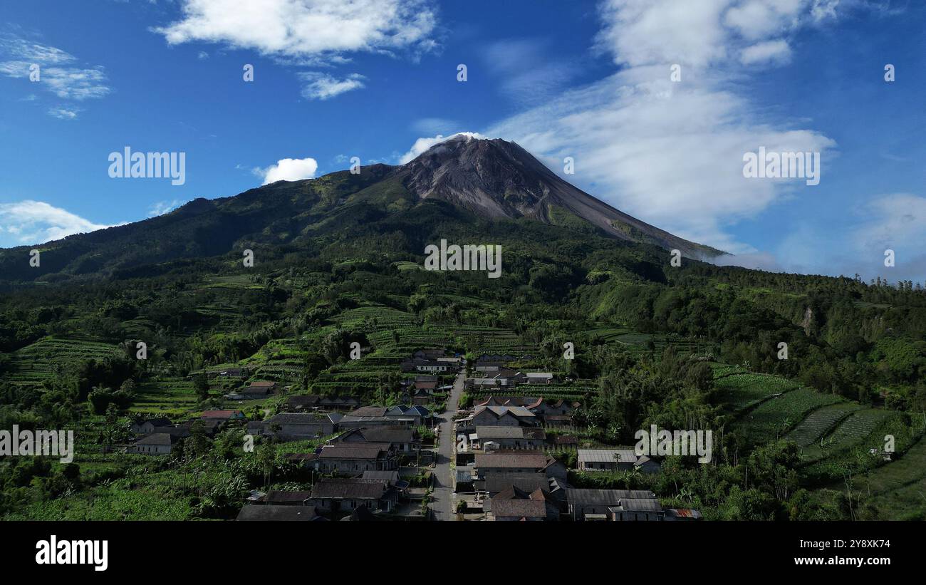 Vista sui droni, le case nel villaggio di Stabelan circondate dall'agricoltura. Il maestoso Monte Merapi offre uno splendido sfondo con un cielo blu nuvoloso Foto Stock