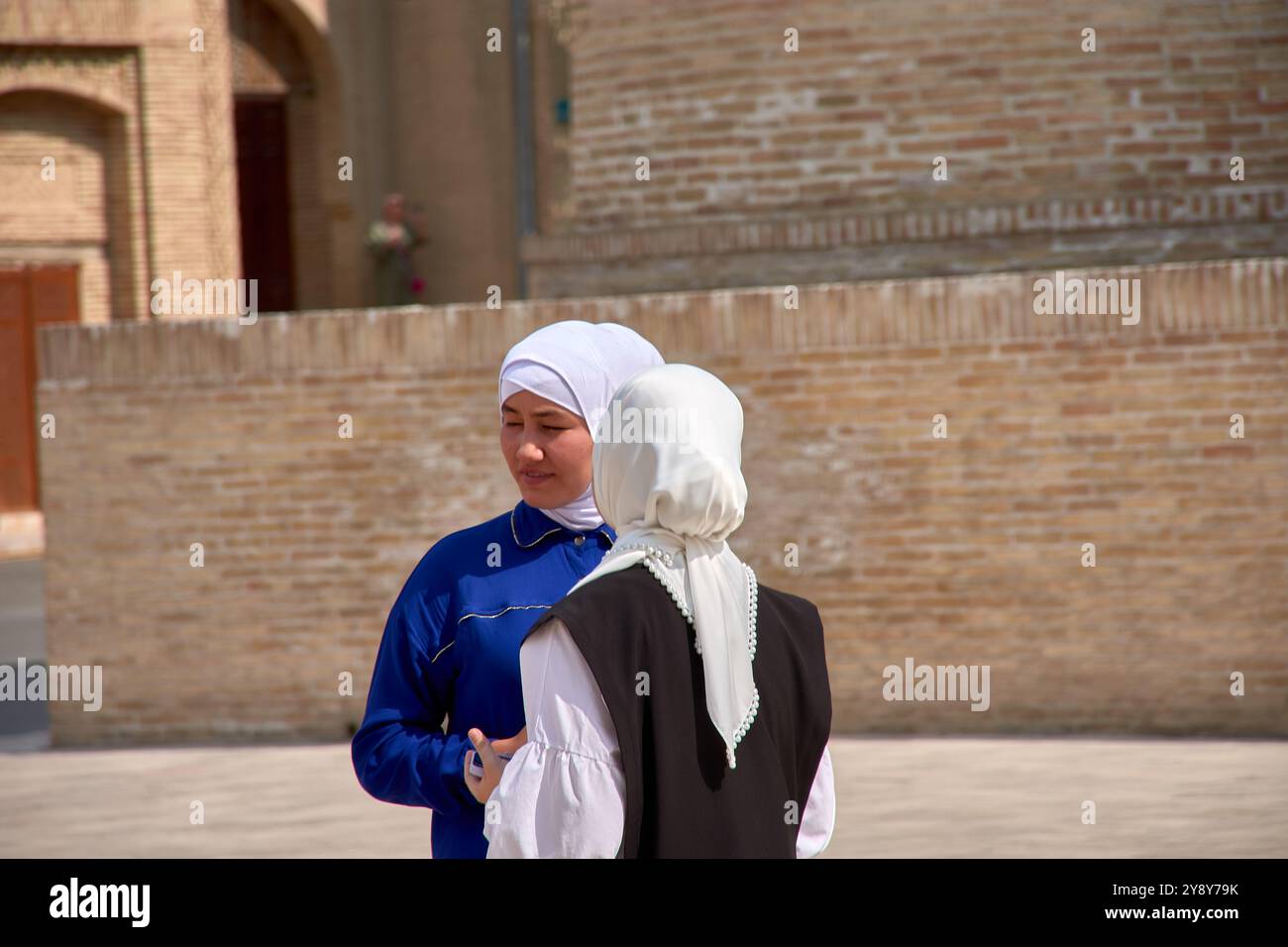 Bukhara, Uzbekistan; 19 settembre 2024: Due giovani donne uzbeke adornate con eleganti veli bianchi, sullo sfondo pittoresco di Bukhara, Uzbekista Foto Stock