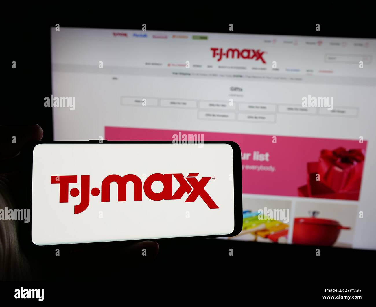 Persona che possiede un telefono cellulare con il logo della società statunitense TJ Maxx sullo schermo davanti alla pagina Web. Mettere a fuoco il display del telefono. Foto Stock