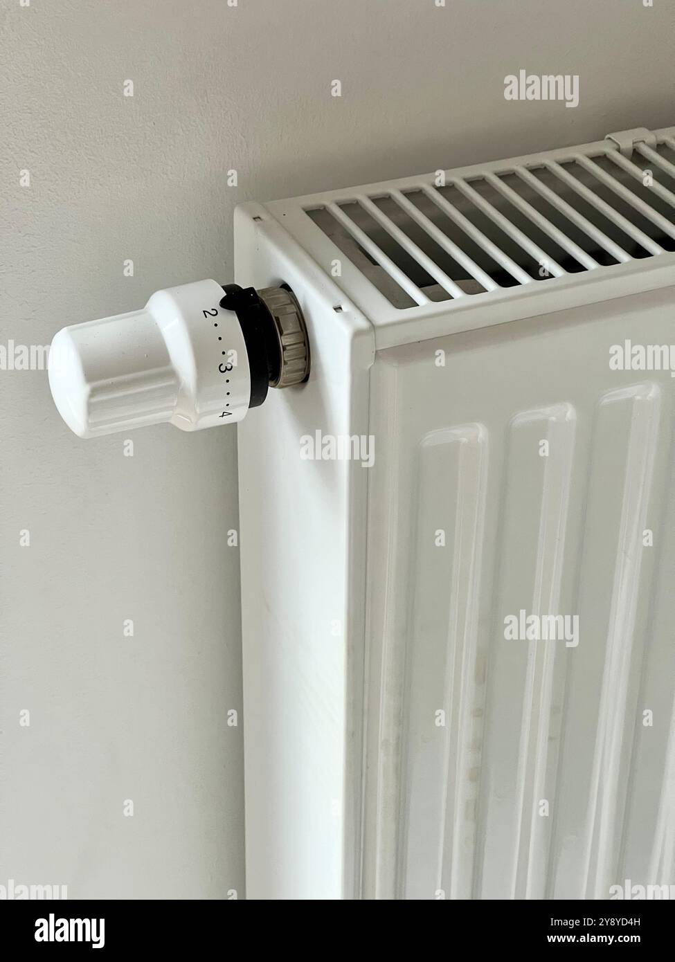 Primo piano verticale di un radiatore e di una valvola bianchi, che evidenziano il design elegante e la consistenza. Perfetto per il riscaldamento domestico, il design degli interni e l'efficienza energetica - Immagine stock catturata con smartphone