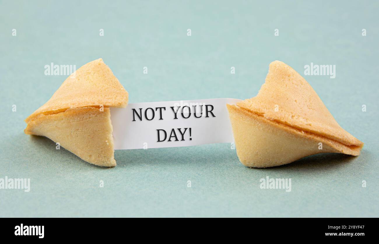 Ho aperto il biscotto della fortuna con un pezzo di carta dentro, una "fortuna" che diceva: NON LA TUA GIORNATA! Sarcastico concetto di sfortuna. Sfondo blu studio. Foto Stock