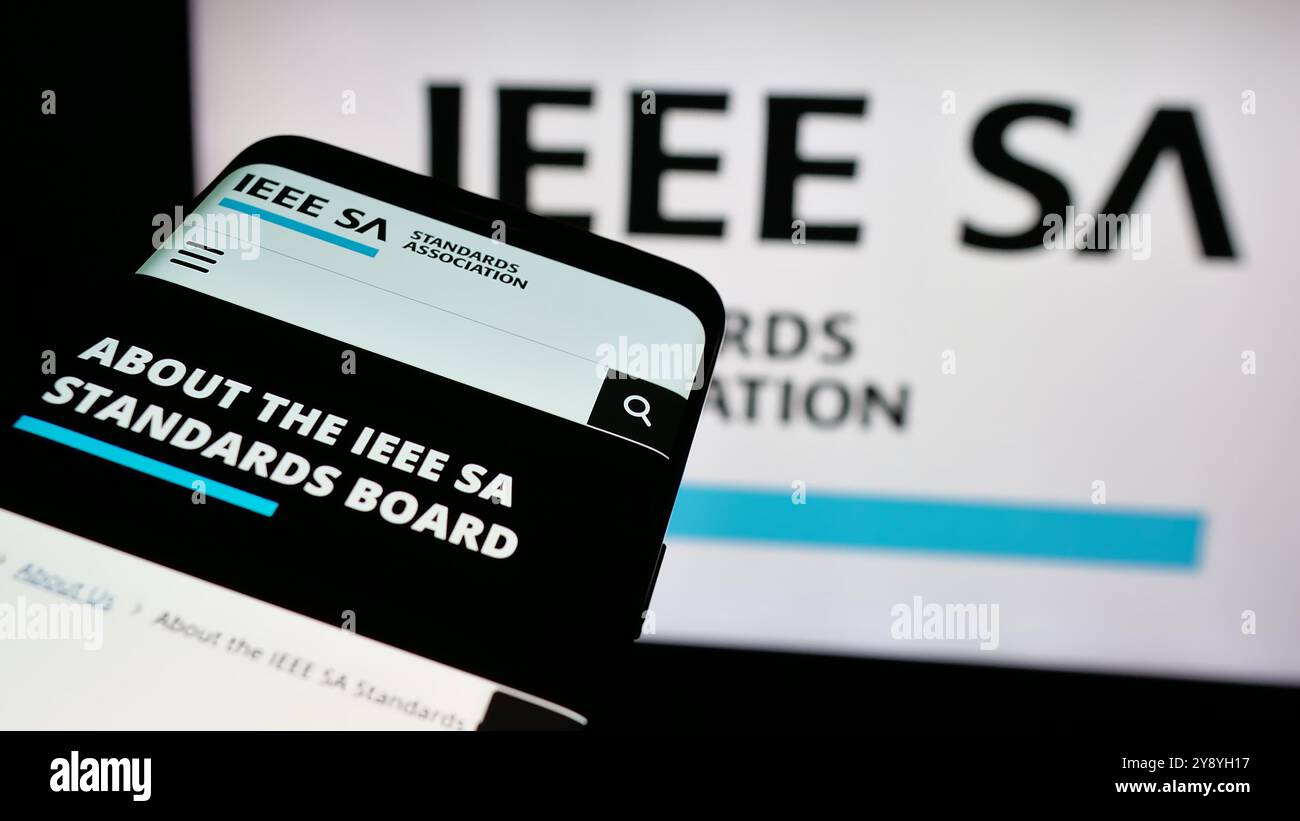 Telefono cellulare con sito Web IEEE Standards Association sullo schermo davanti al logo. Mettere a fuoco in alto a sinistra sul display del telefono. Foto Stock